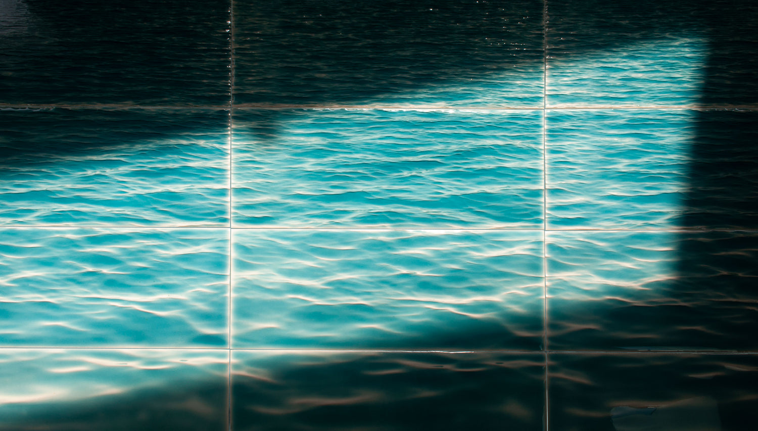 Glossy ceramic tile mural depicting realistic turquoise ocean waves, perfect for luxury coastal bathroom or spa-inspired shower walls. Handcrafted water-inspired tile from Living Walls Tile at livingwallstile.com